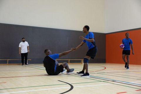 African american players helping teammate up while playing indoor volleyball with coach