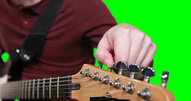 Person tuning an electric guitar with a green screen background, ideal for music tutorials, learning platforms, advertising music equipment, or creating custom video content.