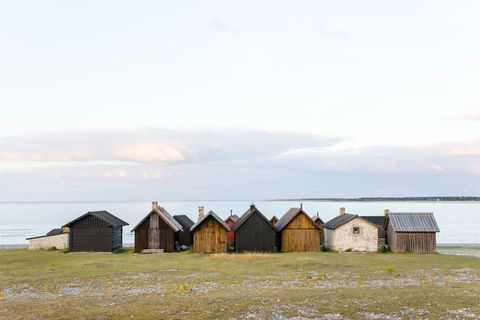 Row of rustic boathouses lining tranquil shoreline with pastel sky and calm sea