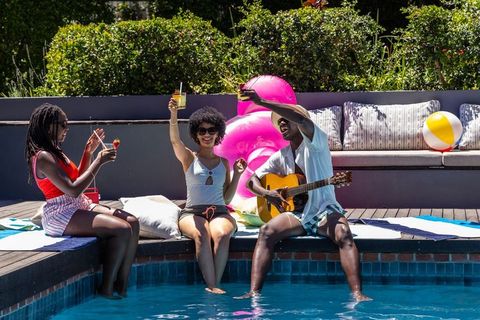 African american friends enjoying poolside party playing guitar and sipping cocktails