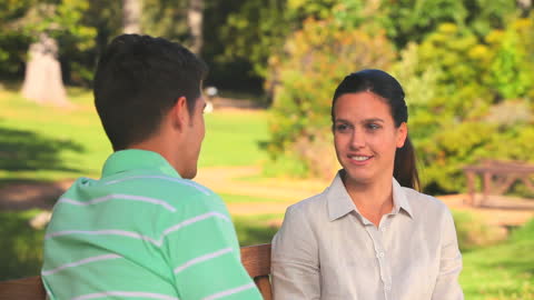 Couple Enjoying a Conversation on Park Bench in Sunlit Garden