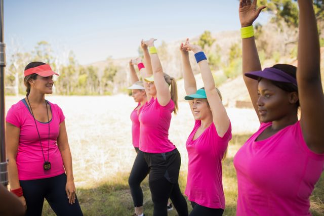 Female trainer instructing a group of women exercising in an outdoor boot camp on a sunny day. Women are wearing sportswear and participating in a group workout, promoting teamwork and an active lifestyle. Ideal for use in fitness blogs, health and wellness articles, and promotional materials for outdoor fitness programs.