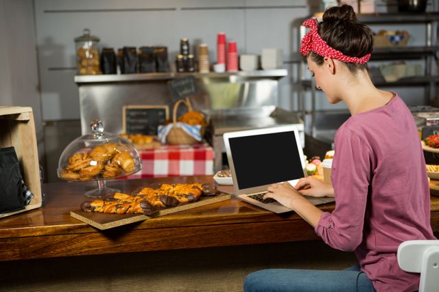Woman using laptop at bakery counter in market
