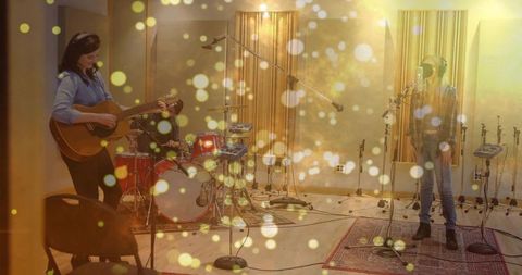 Recording trio performing in studio, guitarist playing acoustic, vocalist singing with red drum kit