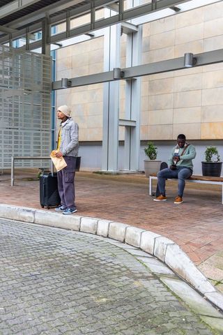 Travelers waiting under modern canopy with wheeled luggage and envelope at urban curb