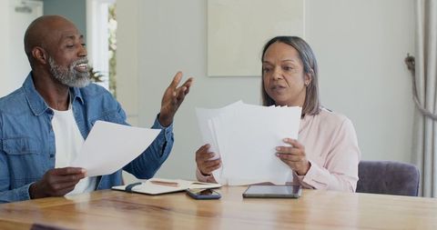 Senior black couple reviewing bills and financial documents at dining table