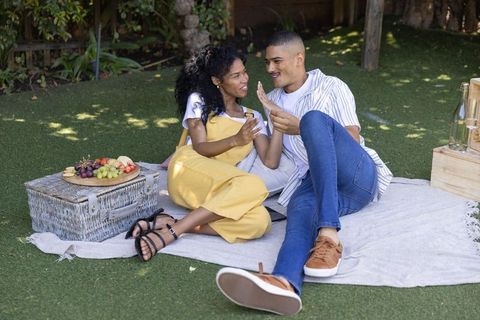 Relaxing young couple sharing intimate backyard picnic, holding hands and laughing
