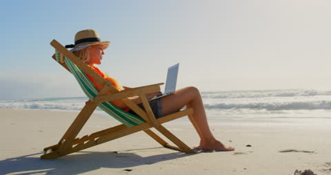 Woman Relaxing on Beach Chair Using Laptop Under Sun