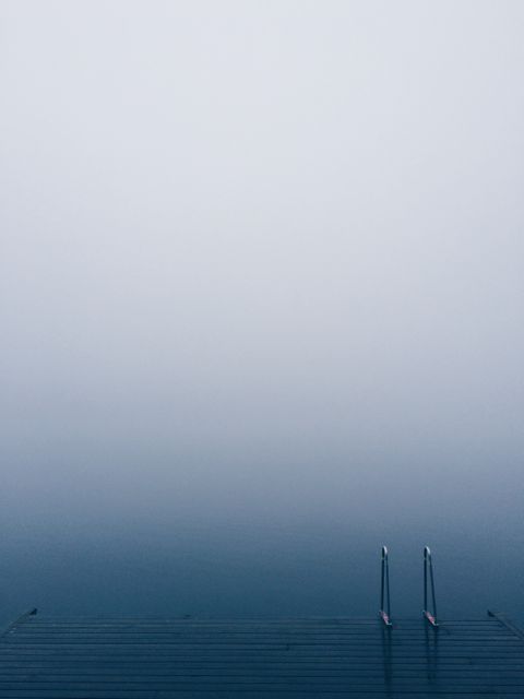 Foggy pier extending over calm lake water on a misty morning. This serene and tranquil scene is perfect for illustrating topics such as peace, solitude, and nature’s beauty. Ideal for travel blogs, relaxation content, and mindfulness resources.