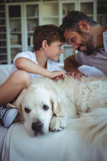 Father and son sitting on sofa with pet dog in living room at home