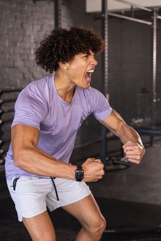 Young man roaring and pumping clenched fists during intense gym workout with battle ropes