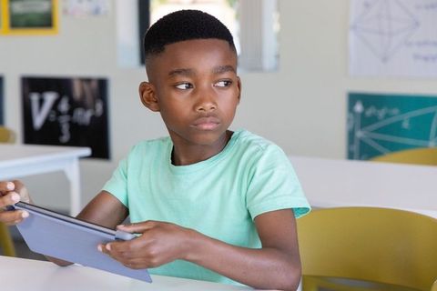 African american schoolboy using tablet in classroom studying math and geometry