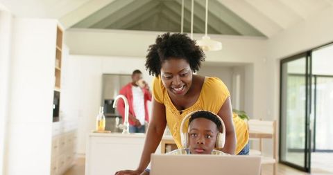 African american mother helping son with laptop and headphones at kitchen island