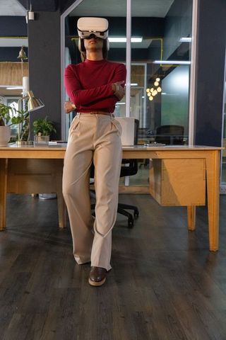Asian woman wearing white vr headset leaning against desk in modern co-working office