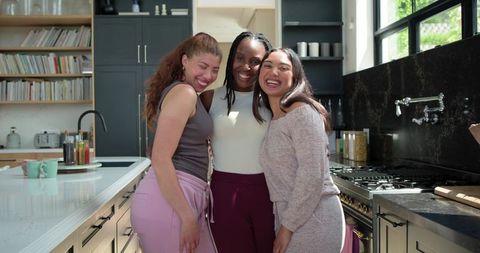 Diverse women laughing and hugging on marble kitchen island in bright modern lifestyle