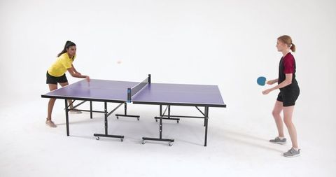 Two diverse female friends playing table tennis in studio
