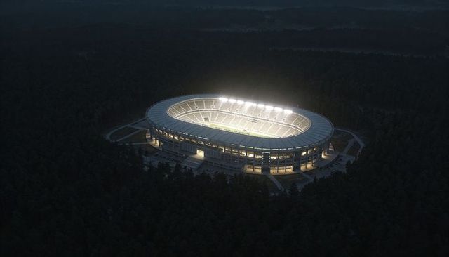 Illuminated oval stadium nestled in forest at night with floodlit pitch and access roads