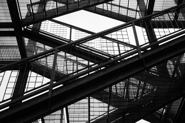 Abstract steel structure with overlapping geometric patterns captured in black and white. Ideal for use in architectural designs, industrial art projects, engineering presentations, and modern decor themes.