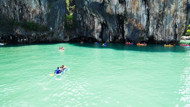 Kayakers exploring clear turquoise waters near towering limestone cliffs. Ideal for use in tourism promotions, adventure blog posts, travel brochures, or social media content highlighting nature excursions and outdoor activities.
