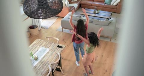 Two women dancing in open-plan living room, friends enjoying casual home lifestyle moment
