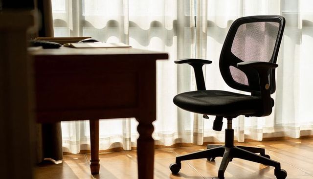 Sunlit office corner with ergonomic mesh chair beside wooden desk, minimalist workspace