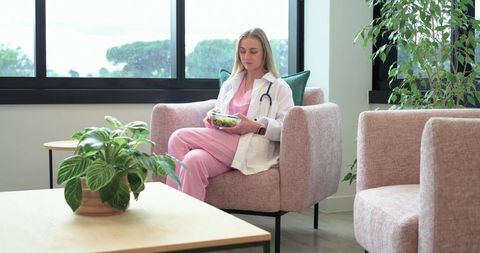Female medical professional taking healthy lunch break in pink scrubs with stethoscope