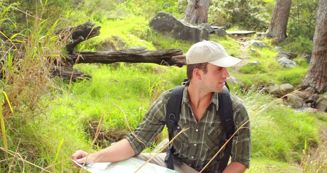 Young man enjoying outdoor adventure, reading map in lush green forest. Ideal for travel blogs, tourism advertisements, hiking gear promotions, and nature exploration articles. Perfect for illustrating themes of exploration, adventure, and outdoor activities.