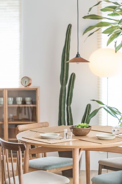 Cozy Scandinavian dining room showcasing minimalist decor with a large cactus, wooden table, chairs and neatly arranged dishes on the table. Ideal for articles on home decor, interior design inspirations, and minimalist lifestyle blogs.
