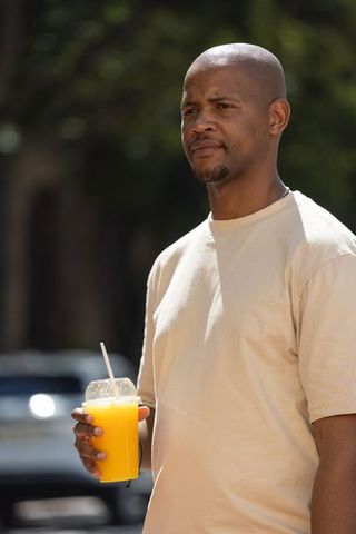 African man holding orange juice cup outdoors in sunlit urban portrait for lifestyle branding