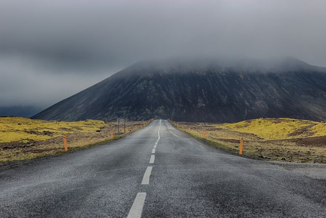 This image shows an empty road disappearing into a foggy mountain landscape. The scenic view features a moody atmosphere with an overcast sky, ideal for themes related to adventure, travel, and exploring remote or desolate locations. Perfect for use in travel blogs, outdoor adventure websites, or landscape photography portfolios highlighting natural beauty and solitude.