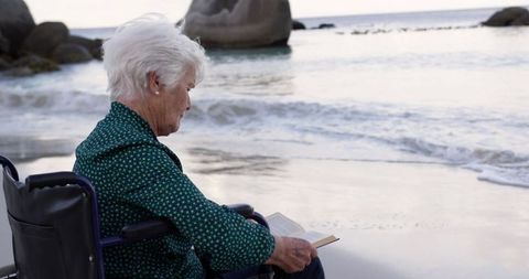 Senior Woman in Wheelchair Reading Book by Peaceful Beach