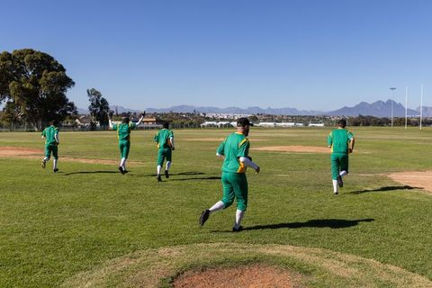 Cricket team running across suburban field in green uniforms with mountain backdrop