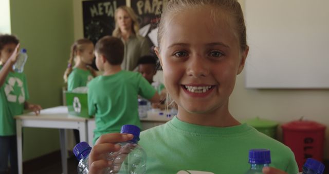 Portrait of happy caucasian girl recycling plastic bottles in elementary school class. Ecology, recycling, environmental awareness, childhood, education, learning and elementary school, unaltered.