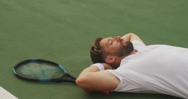 Tied caucasian man lying down with tennis racket, after playing tennis at an outdoor tennis court. Sport, competition, fitness and healthy active lifestyle.