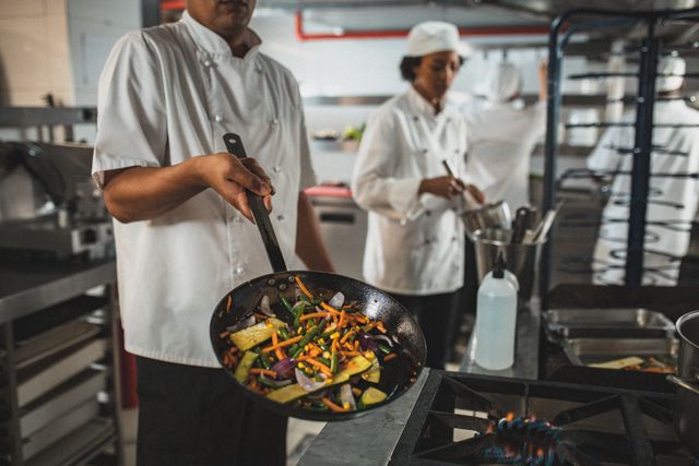 Professional chef preparing a healthy meal with fresh vegetables in a busy restaurant kitchen. Ideal for use in articles or advertisements about culinary arts, healthy eating, restaurant operations, and professional cooking. Can also be used for promoting culinary schools, chef training programs, and kitchen equipment.