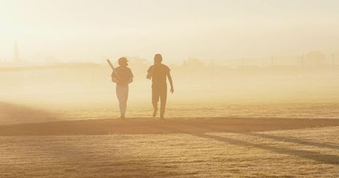Dawn baseball practice walking silhouettes carrying bat across foggy diamond in golden haze