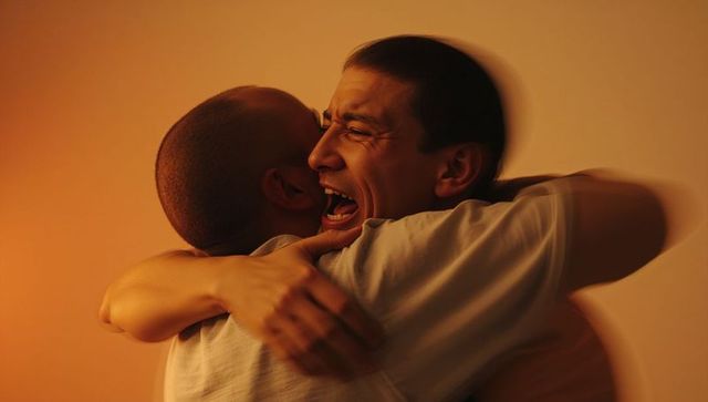 Close-up of two men embracing in warm amber light, conveying raw joy and intimacy