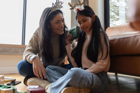 Diverse mother and daughter sharing cozy holiday moment listening to wrapped gift