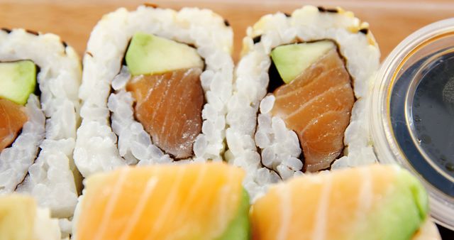 Close-up image of freshly prepared sushi rolls filled with salmon and avocado, placed near a container of soy sauce. Useful for sections on Asian cuisine, restaurant menus, culinary blogs, and recipe illustrations. Visually appealing for emphasizing freshness and quality of ingredients with focus on details.