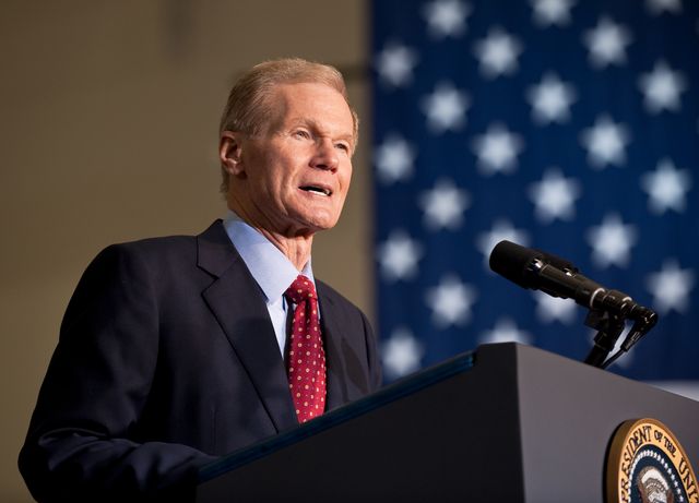 U.S. Senator delivering a speech at a NASA event at Kennedy Space Center. The background features an American flag. This image can be used for topics related to space policy, political events, government speeches, and space exploration initiatives.