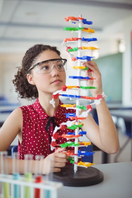 Young schoolgirl wearing safety goggles, attentively working with a colorful molecule model in a science laboratory. Ideal for educational content, STEM programs, school science projects, and promoting hands-on learning in classrooms.