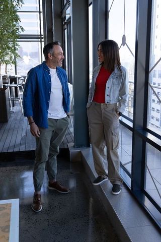 Coworkers chatting by floor-to-ceiling windows in modern office lounge near metal columns
