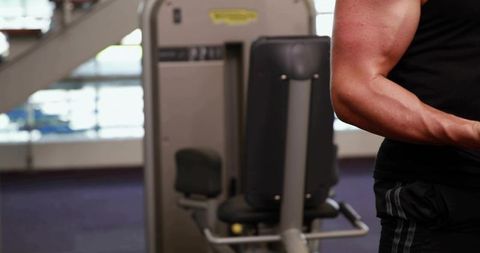 Muscular man flexing biceps at seated gym machine with copy space for fitness branding