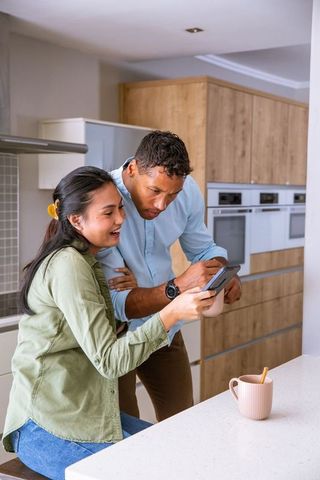 Diverse couple reviewing credit card transaction on smartphone at kitchen