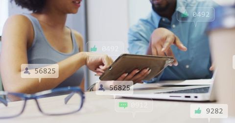 Young professionals collaborating over tablet and laptop with social media engagement icons