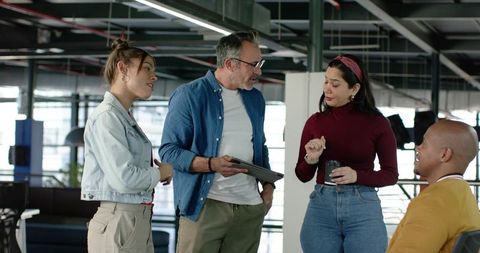 Multicultural team collaborating in modern open-plan workspace with tablet and coffee