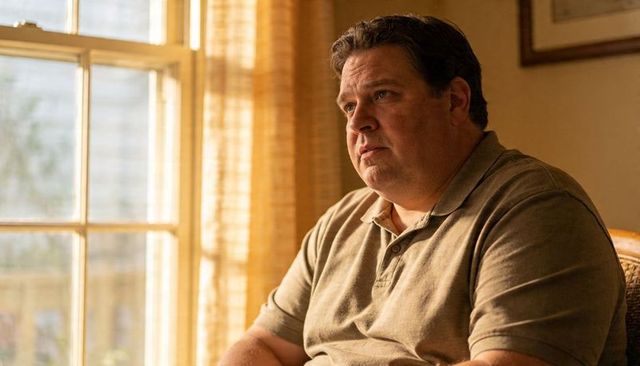 Middle-aged man sitting by sunlit window contemplating life, warm home interior portrait