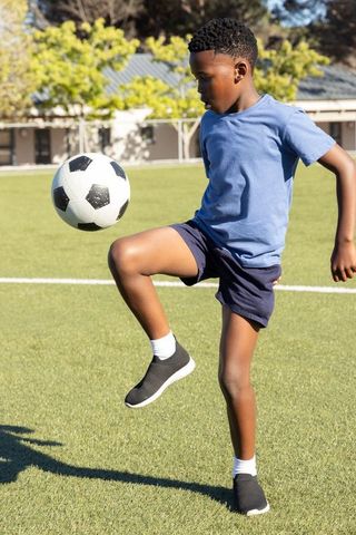 Young african american boy juggling soccer ball on sunlit turf practicing skills