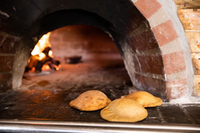 Close up detail of three calzone lying in an oven made from bricks, with a fire in the background