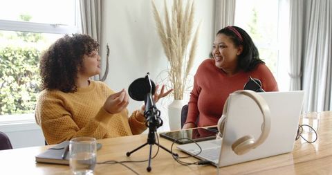 Women cohosts recording podcast at home with laptop, microphone and headphones